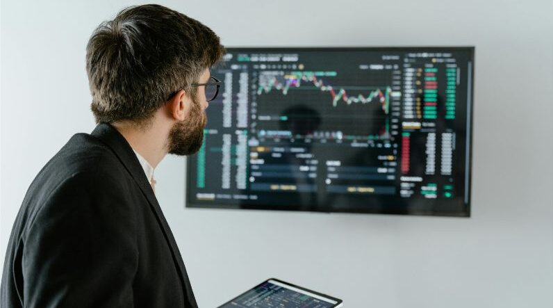 Man in Black Suit Holding a Digital Tablet and Looking At Data On Screen