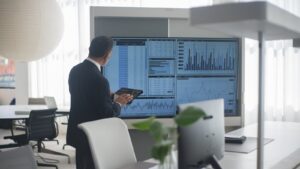Professional in suit analyzing financial data on screens in a modern office setting