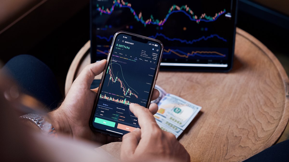 Close-up of a person trading stocks using a smartphone and a tablet.